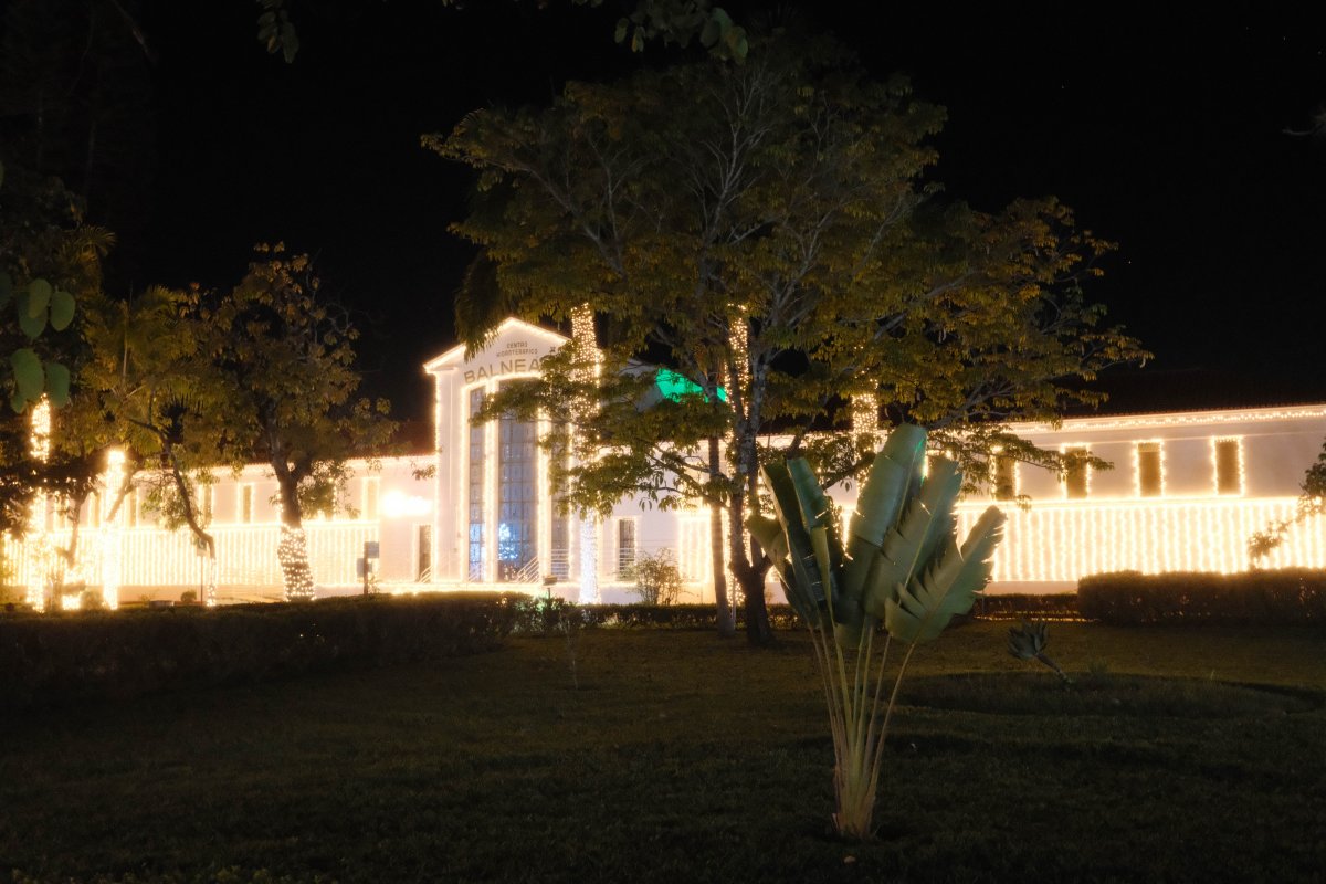 The Balneário in São Lourenço, Minas Gerais, Brazil, illuminated by hundreds of warm Christmas lights at night, with trees and tropical plants surrounding the historic building.