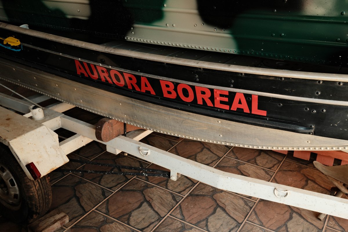 A close-up of a small green boat named Aurora Boreal, resting on a white trailer.
