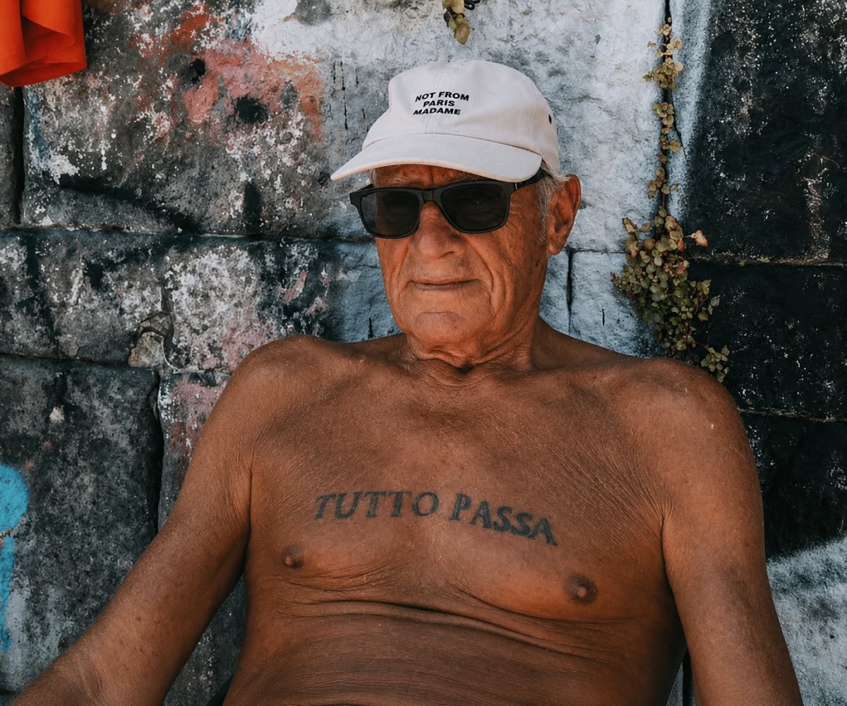 An elderly man wearing a cap, sitting down, with the Italian tattoo “Tutto passa.”