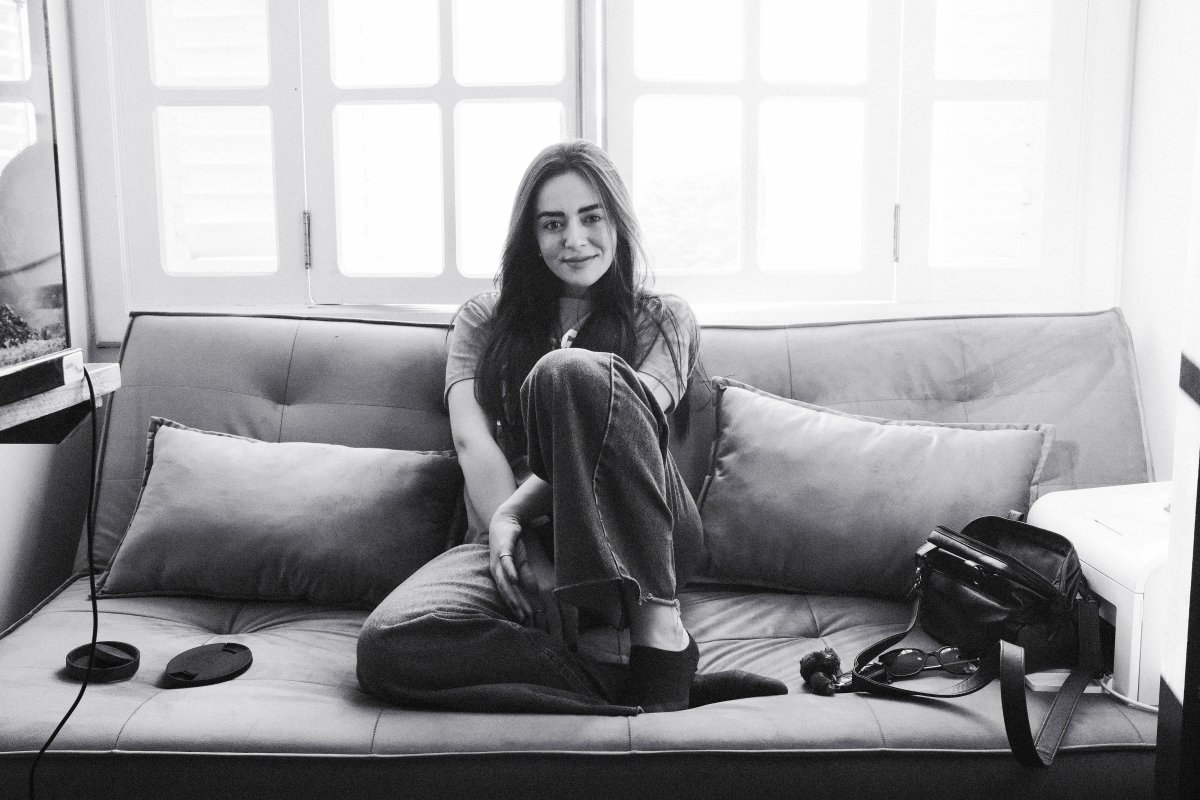 A young woman with long black hair and fair skin, sitting on a sofa and smiling.